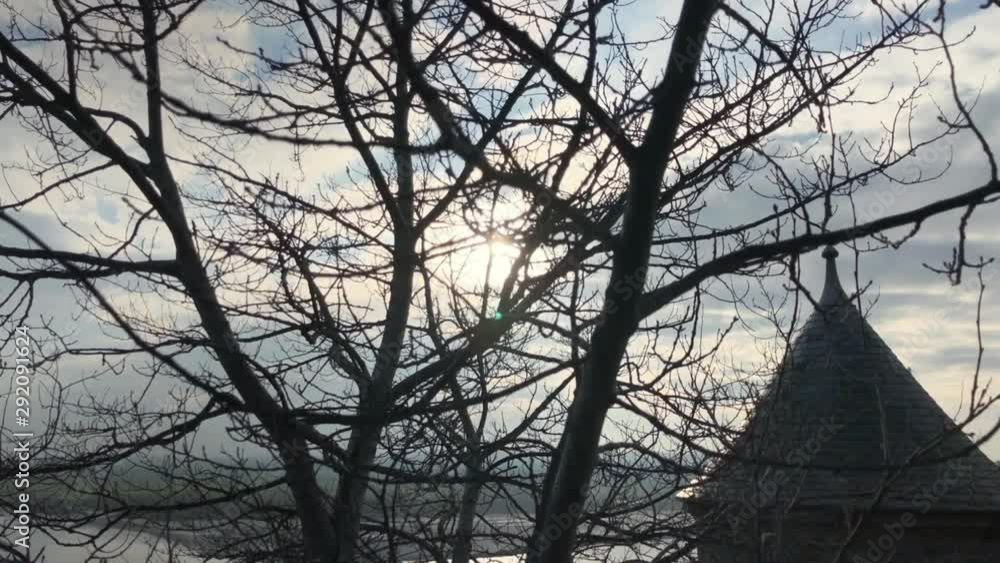 Tree branches and medieval conical roof against cloudy sky and shining sun. Tilt up shot in landscape background. 1080p slow motion stabilized footage. Mont Saint-Michel, France. Tree branches and medieval conical roof against cloudy sky and shining sun. Tilt up shot in landscape background. 1080p slow motion stabilized footage. Mont Saint-Michel, France.