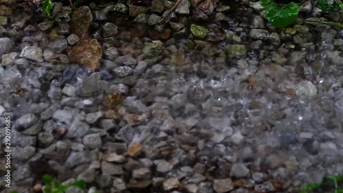 Close up pan across some small rocks in the rain with water running over them photo