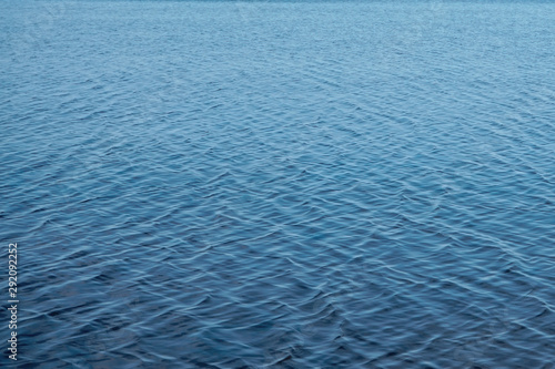 Blurred water background. Texture of small ripples on the water. Saturated blue shades with a light gradient.