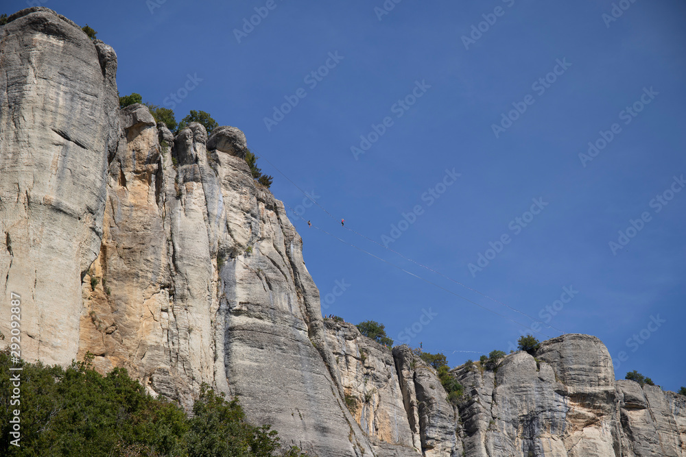 The vertical cliffs of the stone of Bismantova with tightrope walkers and the blue sky in the background.