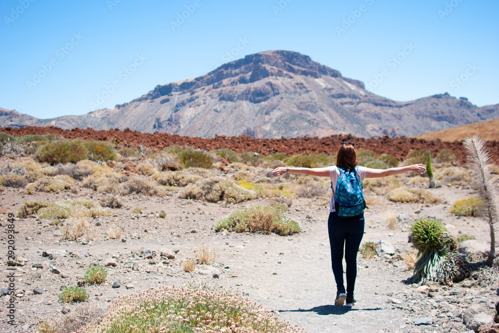 Happy girl with a backpack climbs the slope of the volcano