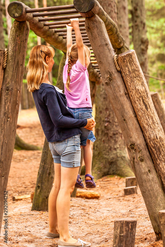 Mother Supporting daughter in the playground with climbing and hanging on a ladder photo