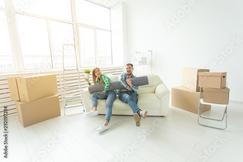 Cheerful joyful young couple charming girl and handsome man holding a box with things and a pot with a plant while moving to a new apartment. Housewarming and mortgage concept. © satura_
