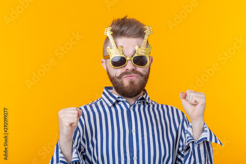 Positive young man with glasses in the form of guitars rejoices against a yellow background. The concept of celebration and parties.