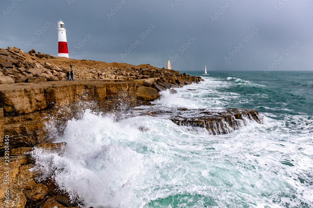 Lighthouse, UK coast with water waves splashing on a cloudy day.