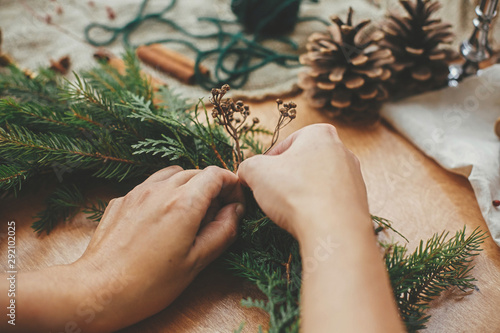 Hands holding herbs and  fir branches, pine cones, thread, berries, cinnamon on wooden table. Christmas wreath workshop. Authentic stylish still life. Making rustic Christmas wreath. photo