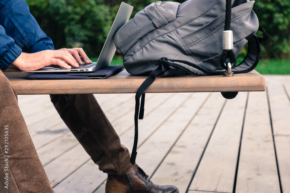 man working on a laptop outdoors on a park bench, near a backpack man working on a laptop outdoors on a park bench, near a backpack