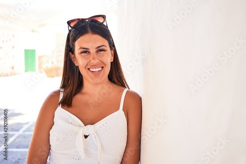 Beautiful girl leaning on white wall, young friendly woman smiling happy on a sunny day of summer