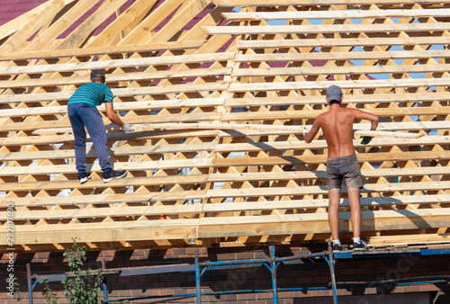 Workers are building the roof of the house from wood