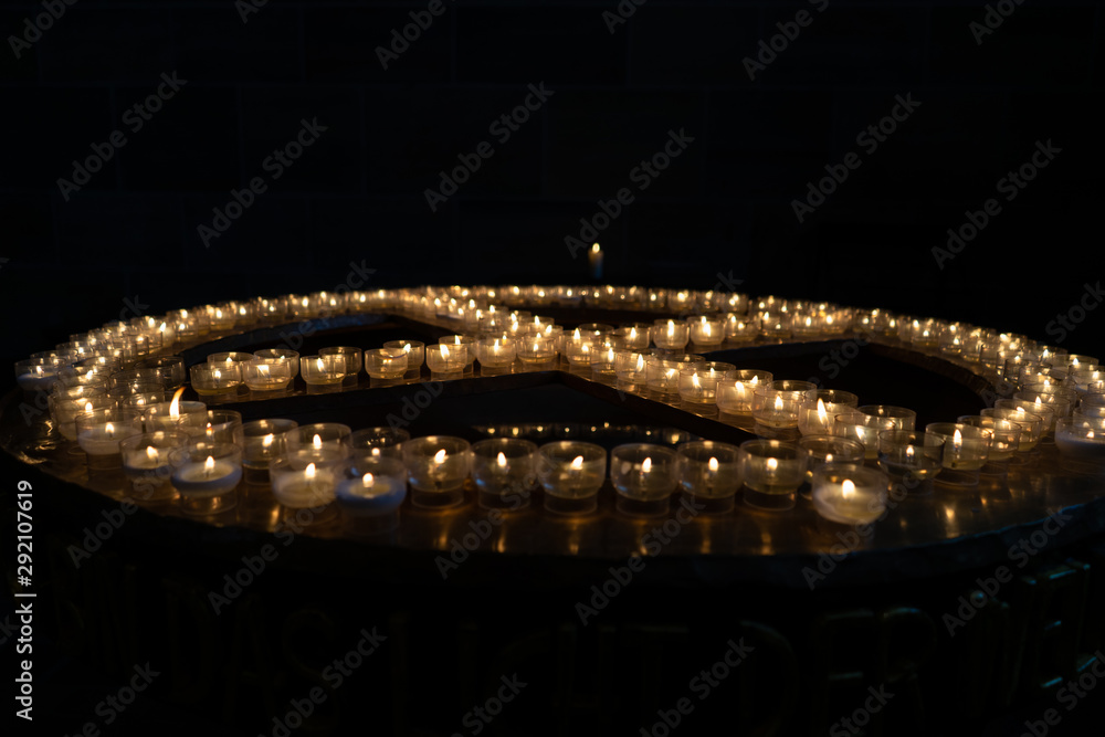 Candles in Church, group of burning candles at a black background. The shape of the cross of burning candles in the ancient temple