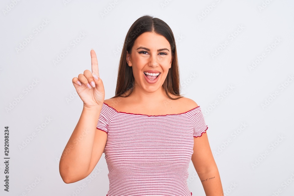 Portrait of beautiful young woman standing over isolated white background showing and pointing up with finger number one while smiling confident and happy.