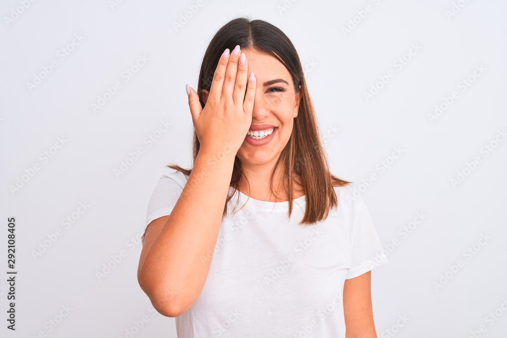 Portrait of beautiful and young brunette woman standing over isolated white background covering one eye with hand, confident smile on face and surprise emotion. Portrait of beautiful and young brunette woman standing over isolated white background covering one eye with hand, confident smile on face and surprise emotion.