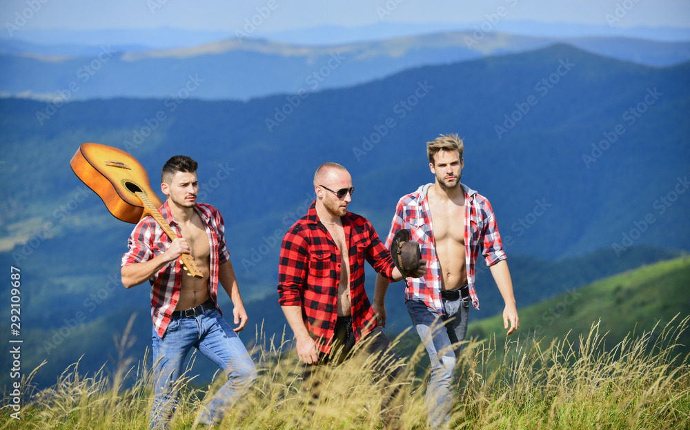 Group of young people in checkered shirts walking together on top of mountain. Men with guitar hiking on sunny day. Tourists hiking concept. Hiking with friends. Long route. Enjoying freedom together Group of young people in checkered shirts walking together on top of mountain. Men with guitar hiking on sunny day. Tourists hiking concept. Hiking with friends. Long route. Enjoying freedom together