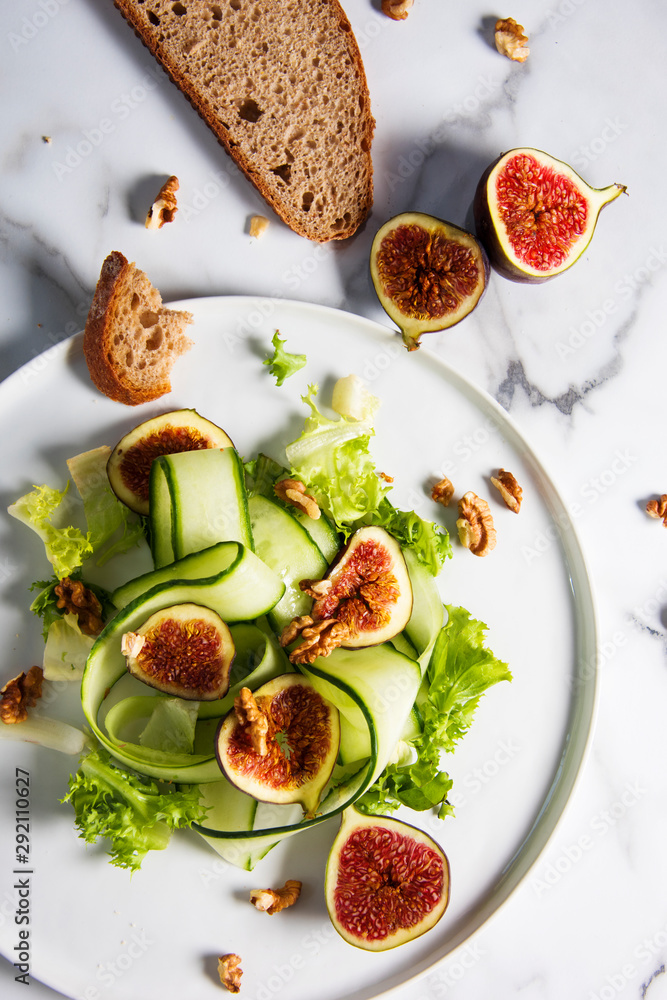 Green salad with figs on white plate and white marble patterned background. Gourmet conception. Green salad with figs on white plate and white marble patterned background. Gourmet conception.