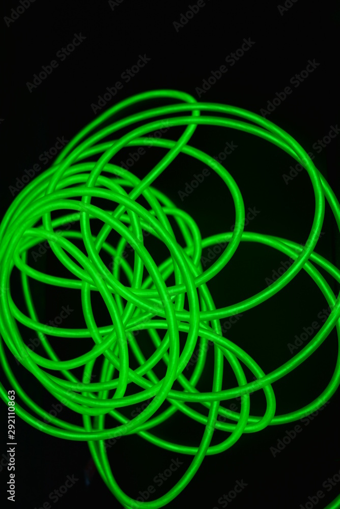 Toxic green luminous wires with different shapes and structures. A web of lime fiber and unusual circles located on a black glossy surface. Toxic green luminous wires with different shapes and structures. A web of lime fiber and unusual circles located on a black glossy surface.