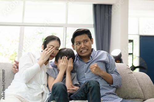 young family, father, mother and son watching TV feeling scared together in living room, happy family concept