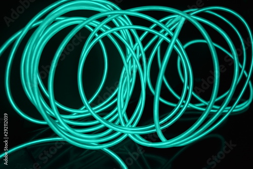 Unusual bright wires made of turquoise-colored material glowing at night. Chaotic sky blue wires, light guide electroluminescent wires, electroluminescence are located on a glossy black surface. photo