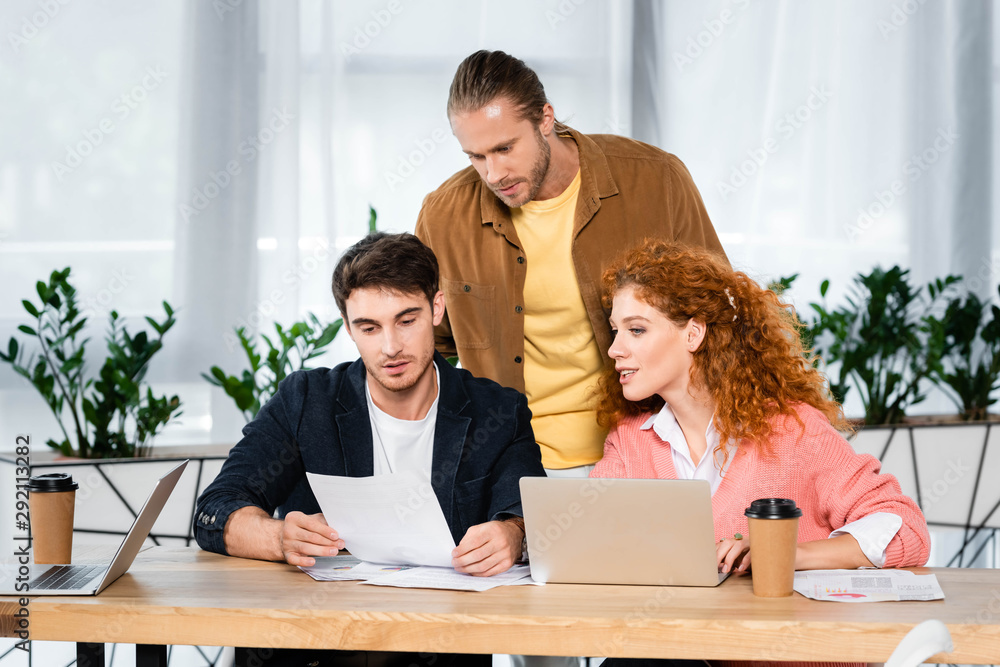 three friends doing paperwork and sitting at table in office three friends doing paperwork and sitting at table in office