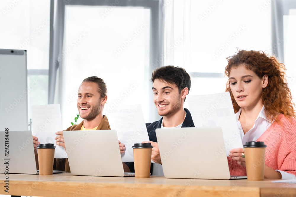 three smiling friends sitting at table and doing paperwork three smiling friends sitting at table and doing paperwork