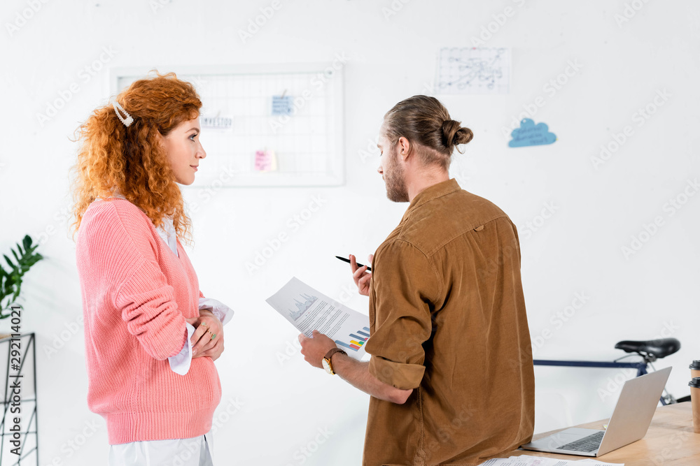 Fototapeta premium back view of two friends talking and doing paperwork in office