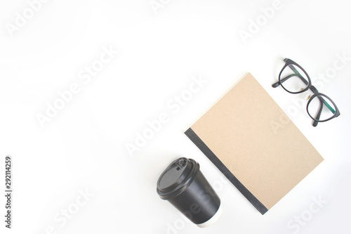 The white workspace of the notebook, coffee and eye glasses placed on the background of the work desk with copy space.