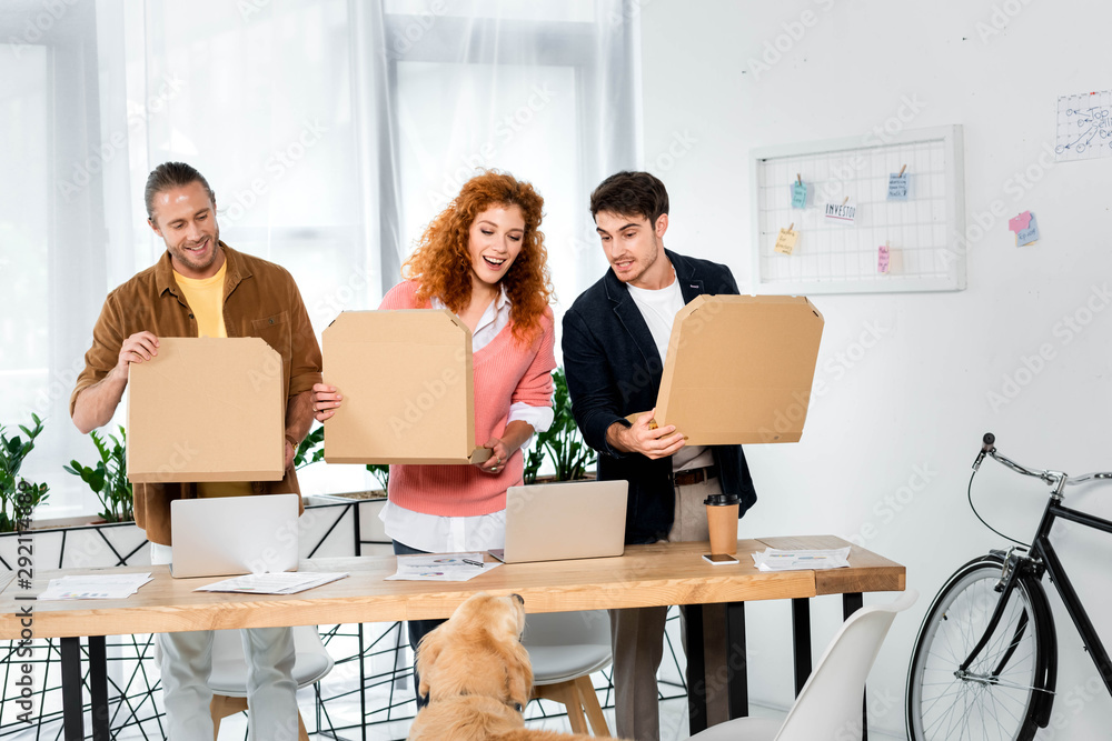 three smiling fiends holding boxes with pizza in office three smiling fiends holding boxes with pizza in office