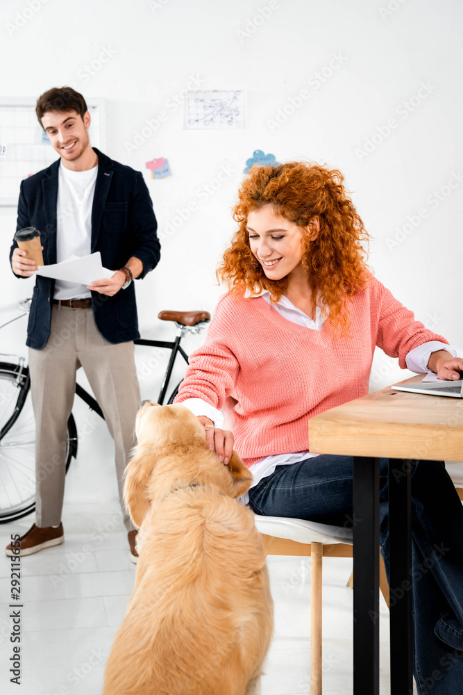 handsome man looking at attractive woman stroking cute golden retriever in office handsome man looking at attractive woman stroking cute golden retriever in office