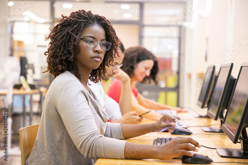 African American adult student working in computer class. Line of man and women in casual sitting at table, using desktops, typing. Staff training concept photo