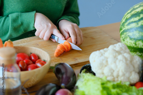 girl cuts a carrot with a knife to make a salad. 