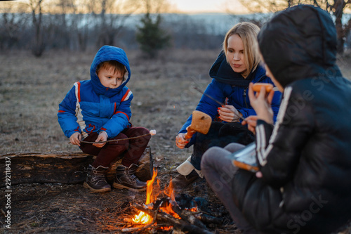 Mother, daughter and son are sitting around the campfire on a picnic. Family outdoor recreation. Travel, hike, halt concept. © Konstiantyn Zapylaie