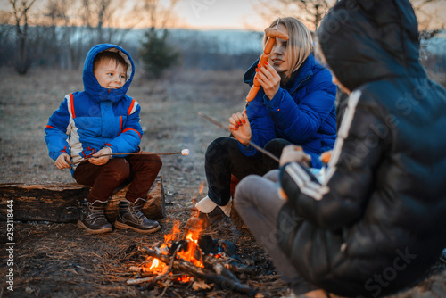 Mother, daughter and son are sitting around the campfire on a picnic. Family outdoor recreation. Travel, hike, halt concept.