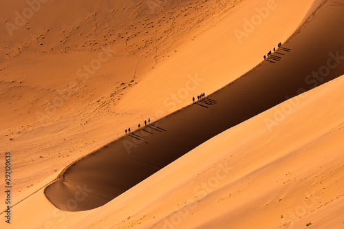 Fototapeta Naklejka Na Ścianę i Meble -  Aerial view group of people walking on the sand dune in the desert and sun gradually create beautiful scene.