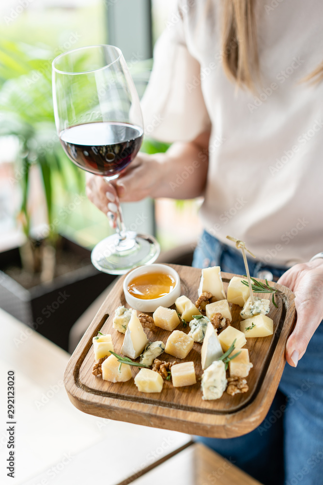 Girl holding glass red wine and wooden plate with cheese. Delicious cheese mix with walnuts, honey. Tasting dish on a wooden plate. Food for wine. Girl holding glass red wine and wooden plate with cheese. Delicious cheese mix with walnuts, honey. Tasting dish on a wooden plate. Food for wine.