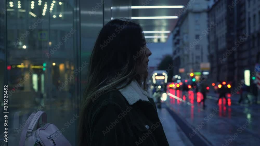 A girl stands at a tram stop. In the center of Moscow, a girl in autumn rainy weather is waiting for transport. Evening movie. A girl stands at a tram stop. In the center of Moscow, a girl in autumn rainy weather is waiting for transport. Evening movie.