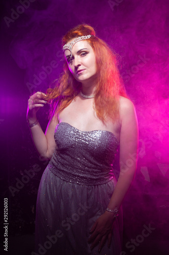 Mature plus size red hair woman in grey evening dress posing on dark smoke background ready for halloween.