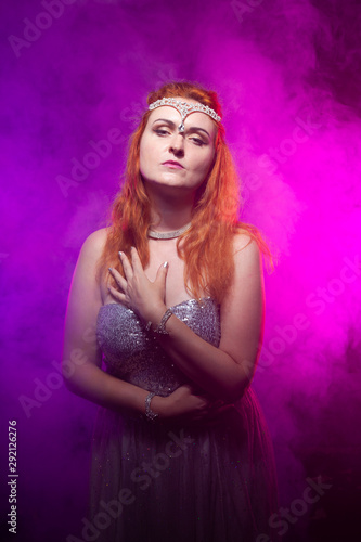 Mature plus size red hair woman in grey evening dress posing on dark smoke background ready for halloween.