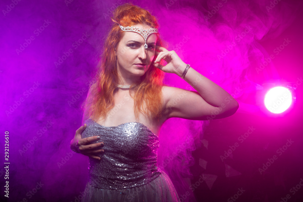 Naklejka premium Mature plus size red hair woman in grey evening dress posing on dark smoke background ready for halloween.