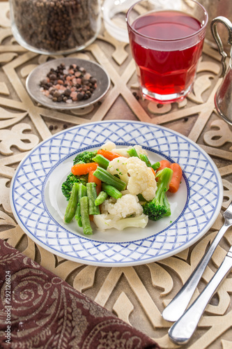 Mixed vegetables cauliflower, broccoli, bean and carrots on white plate and glass of red drink on oriental wooden table