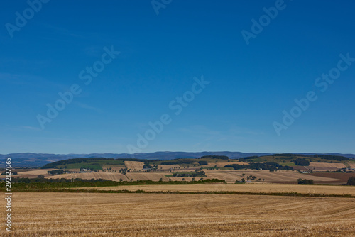 The fields and farmland on the lower slopes of the Strathmore Valley on a bright  clear Septembers day with isolated Farm buildings in the distance 