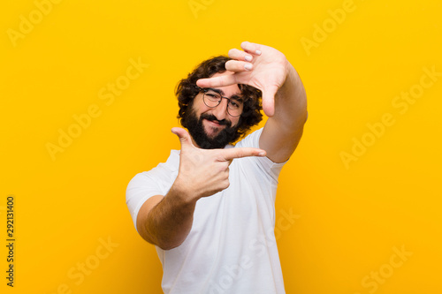 young crazy man feeling happy, friendly and positive, smiling and making a portrait or photo frame with hands against yellow wall