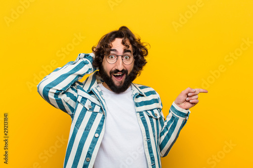 young crazy man laughing, looking happy, positive and surprised, realizing a great idea pointing to lateral copy space against yellow wall