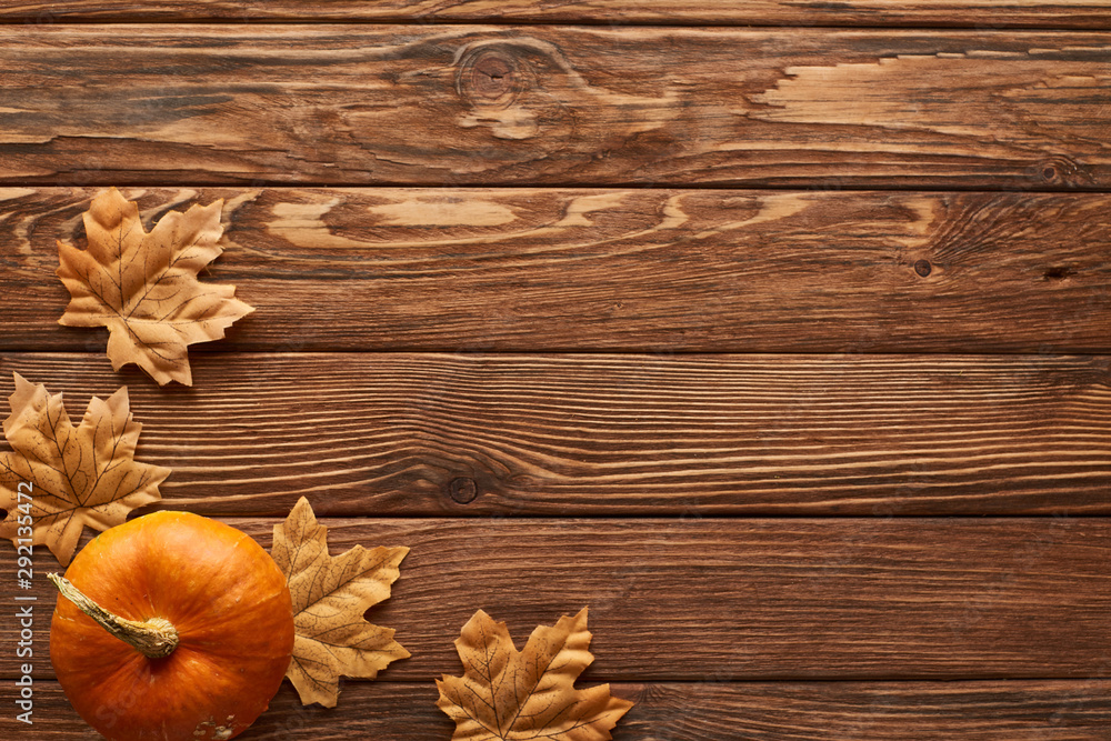 top view of small pumpkin on brown wooden surface with dried autumn leaves top view of small pumpkin on brown wooden surface with dried autumn leaves