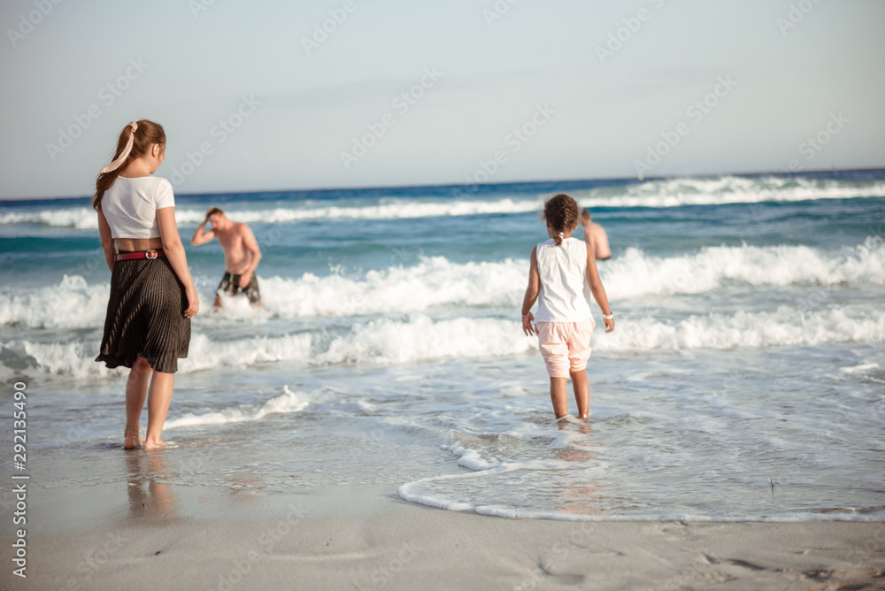 Family walking on the evening beach during sunset. Child with mom.