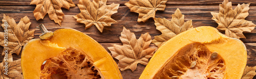 panoramic shot of pumpkin halves on brown wooden surface with dried autumn leaves