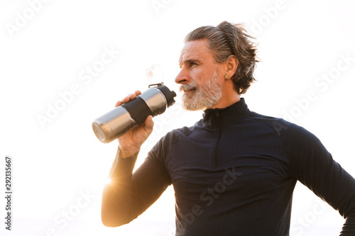 Image of sporty elderly man drinking water while working out