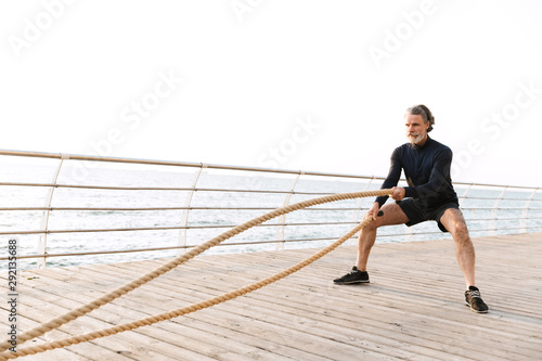 Image of strong old man doing exercise with battle ropes