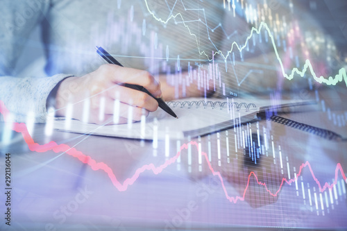 Hands writing information about stock market in notepad. Forex chart holograms in front. Concept of research. Multi exposure