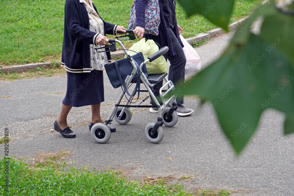 Anziana signora e badante camminano in un parco con il deambulatore