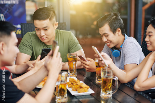 Group of Asian friends communicating online using their mobile phones while they sitting in cafe and drinking beer