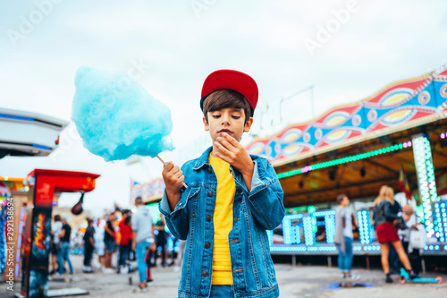 Adorable young boy standing in amusement park and eating blue candy floss